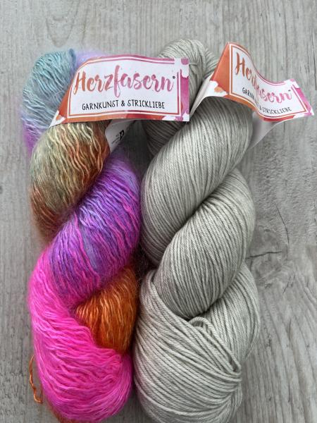 Zwei Stränge handgefärbte Wolle: links Herzfasern No. 50 „Velvet Flower“ in Pink, Lila, Türkis und Gold mit Mohairstruktur, rechts Herzfasern No. 11 „Bergkristall“ in kühlem Naturweiß mit leichtem Graustich auf glatter Merinobasis. Fotografiert auf hellem